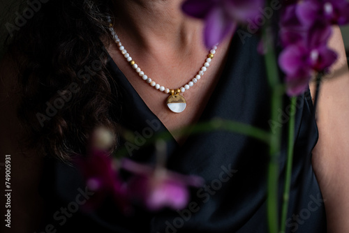 Woman in black satin dress with beautiful white necklace. Pearl necklace on a woman neck with a mother-of-pearl and gold pendant,  and fuksia orchid. Concept: gift, celebrating, affection, love