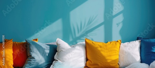 A collection of pillows is neatly arranged on top of a bed, against a vibrant blue wall background, creating a cozy and inviting atmosphere. The pillows are different sizes and colors, adding a touch © Emin