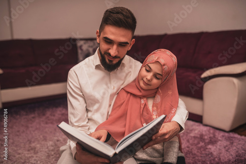 Happy Muslim famliy at home, young father and child daughter together reading a Quran during Ramdan photo