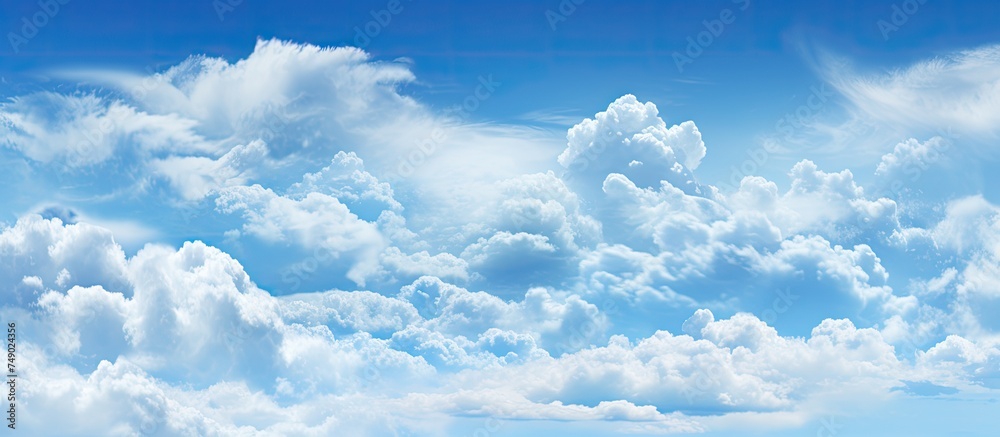 A plane is seen flying through a cloudy blue sky, leaving a trail in its wake. The clouds create a dramatic backdrop against the deep blue hues of the sky.
