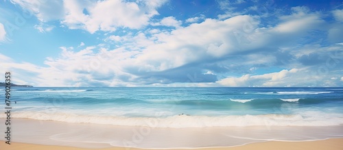A beach scene with waves crashing onto the shore under a cloudy blue sky. The waves are depicted in motion, adding a dynamic element to the serene landscape.