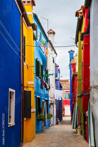 Bright traditional colorful buildings on Burano island, Venice, Italy. Picturesque narrow old street with fabulous colorful houses and drying laundry overhead