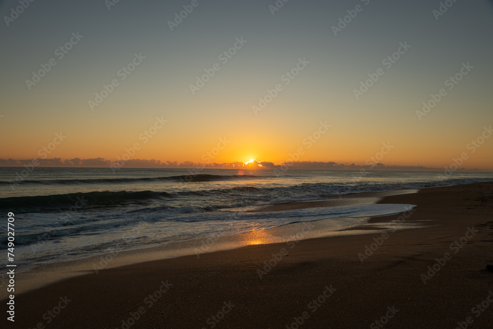 Sunrise on a Florida beach, sea foam on shore, clouds above the horizon