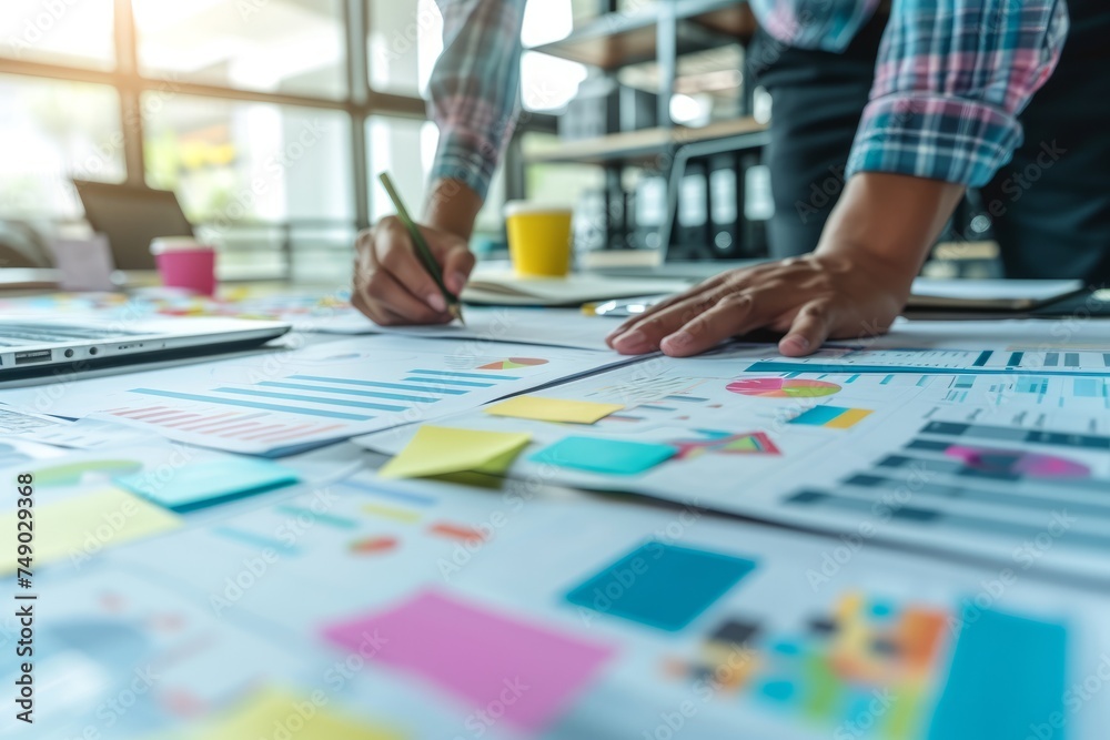 An unrecognizable man writes on a piece of paper between charts and diagrams and colourful sticky notes in his office An unrecognizable man writes on a piece of paper between charts and diagrams and colourful sticky notes in his office