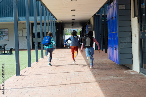 Three children are running through a school corridor with lockers on the right, with copy space