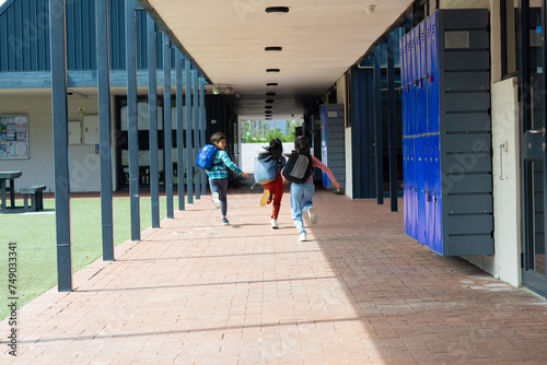 Three children are running through a school corridor with backpacks, with copy space