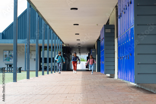 Three students walk through a school corridor lined with blue lockers with copy space