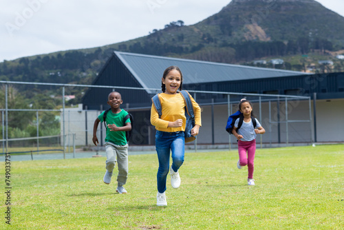Three children are joyfully running across a grassy field during the day in school