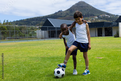 Biracial boy and African American boy play soccer outdoors in school with copy space