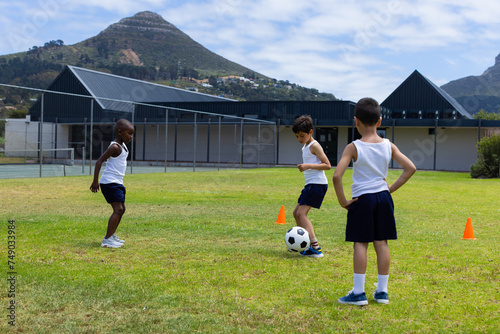 Biracial and African American boys play soccer outdoors at school, with mountains in the background