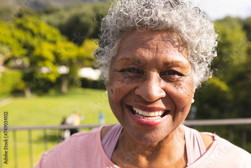 Senior biracial woman with curly gray hair smiles warmly outdoors