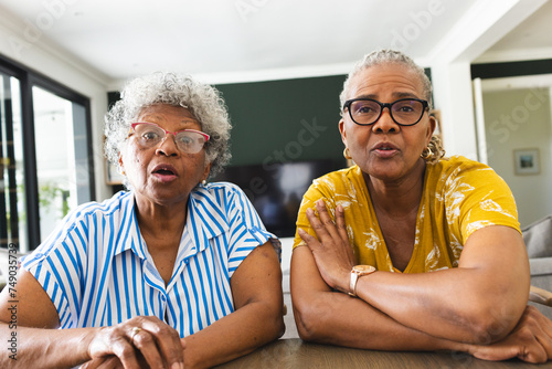 Senior African American woman and senior biracial woman sit together indoors on video call at home photo