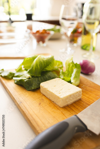 A block of cheese and fresh lettuce are on a cutting board with a knife nearby