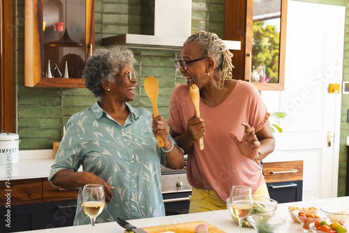Senior African American woman and senior biracial woman share a joyful moment in a kitchen
