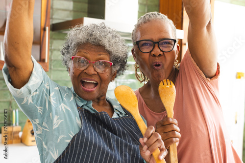Senior African American woman and senior biracial woman celebrate with kitchen utensils