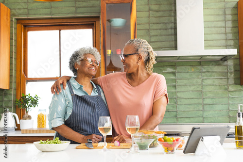 Senior African American woman and senior biracial woman share a warm moment in a sunny kitchen