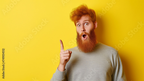 Homem ruivo barbudo com um dedo levantado e expressão de impressionado isolado no fundo amarelo 