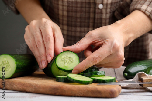 Woman putting slice of fresh cucumber onto cutting board, closeup