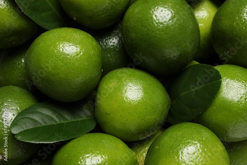 Fresh ripe limes and leaves as background, top view