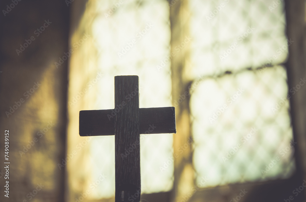 Silhouette of cross, symbol of Christian faith, inside a sacred church in front of a beautiful antique stained glass window. Warm light. Easter holy week Good Friday concept.