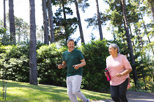 Senior biracial couple is jogging together in a sunny park