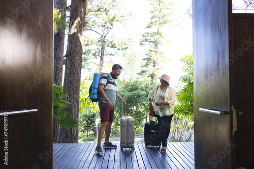 Senior biracial couple with luggage entering a wooden-floored vacation home photo