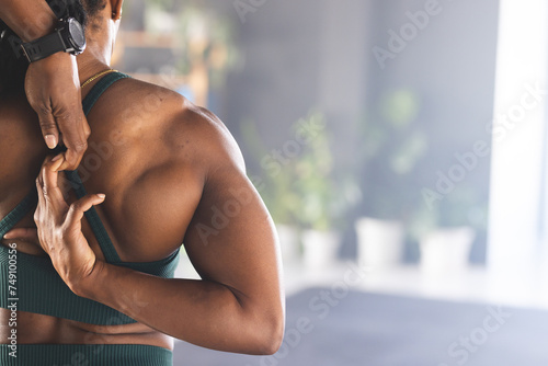 Strong biracial woman experiencing shoulder pain, wearing a teal sports top, with copy space photo