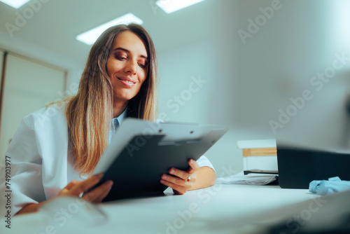 Doctor Holding Paper Records Working in her Office. Happy general practitioner reading anamnesis from a medical document 