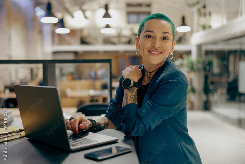 Ταπετσαρία Smiling tattooed female freelancer with green short hair working on laptop while