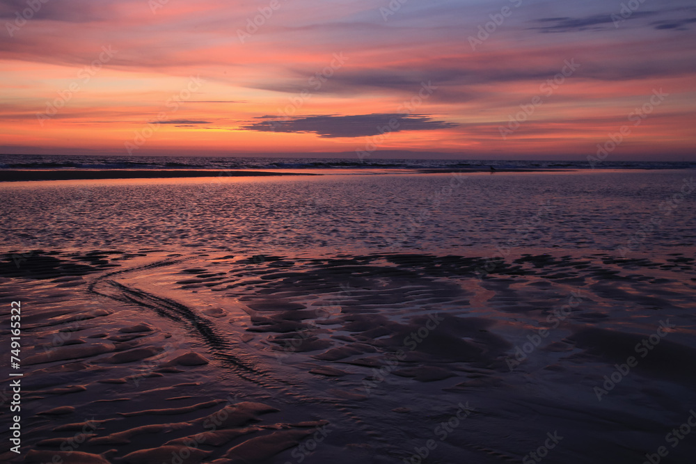 sunset sky is reflecting in the low tide draining waters of a beach in Sylt Island, Germany