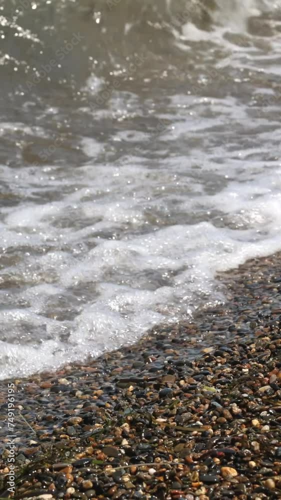 Waves Wash Over A Pebble Beach With Small Stones And Rocks. Sea Surf On A Summer Day On The Beach. The Waves Of The Sea In Focus. Vertical. Waves Wash Over A Pebble Beach With Small Stones And Rocks. Sea Surf On A Summer Day On The Beach. The Waves Of The Sea In Focus. Vertical.