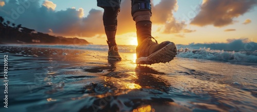 An amputee using a prosthetic limb walks along the shore  with waves gently lapping at their feet during a golden sunset.