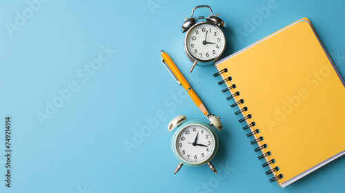 Notebook, alarm clock, pen on blue background.