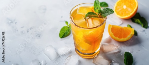 A glass of refreshing orange juice garnished with fresh mint leaves and filled with ice cubes on a white background.