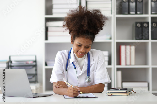 African female doctor in office doing paperwork and writing prescriptions.