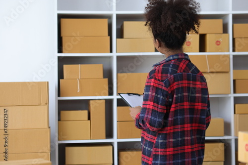 Young African woman starting an online shopping business from home is preparing packages to deliver to customers following internet orders.