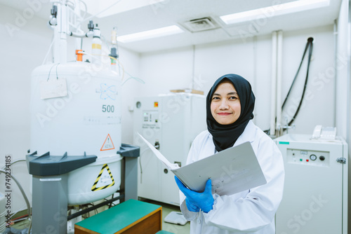 Muslim Scientist Holding Logbook, Standing Next to NMR Machine in Laboratory