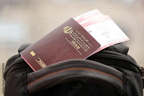 Red Islamic Republic of Iran passport with airline tickets on touristic backpack close up. Tourism and travel concept