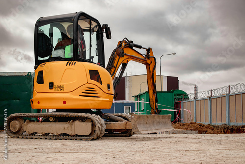 A mini excavator rams the ground with a vibrating plate. Laying of underground sewer pipes and communications during construction. soil compaction. Earthworks, excavation. photo