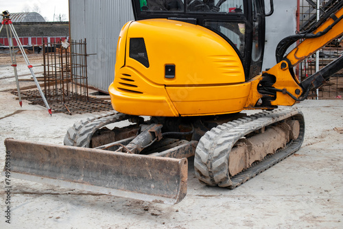 A mini excavator rams the ground with a vibrating plate. Laying of underground sewer pipes and communications during construction. soil compaction. Earthworks, excavation.