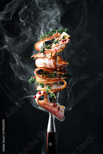 Slices of smoked bacon on a metal fork. On a black background, close-up.