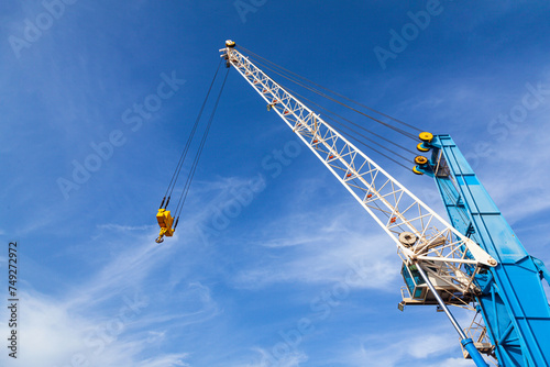 Top of port crane with a stabilizer and a hook against a blue sky.