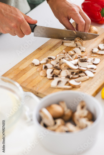 Hands are slicing mushrooms on a wooden cutting board with a kitchen knife