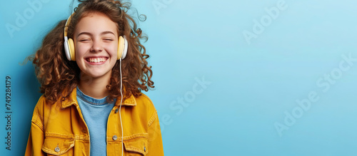 Happy funny teen girl wearing headphones, listening music. Blue background.