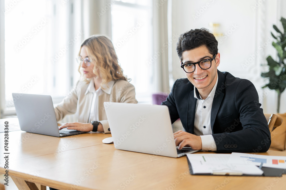 Smiling professionals working on laptops in a bright, modern office space. Smiling professionals working on laptops in a bright, modern office space.