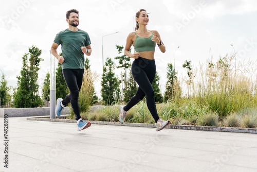 Active couple jogging together in an urban park, with tall grass and modern design.