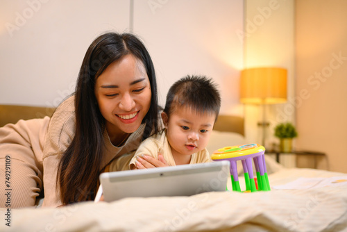 Happy asian mother and her adorable baby boy using digital tablet on the bed