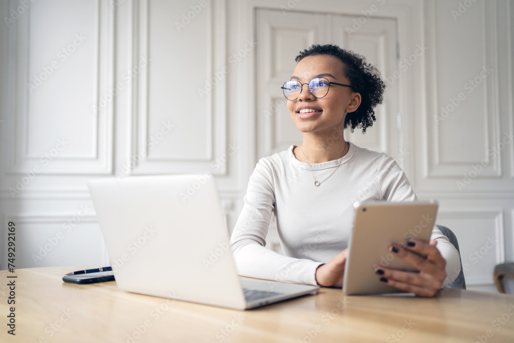 Smiling young woman with glasses using a tablet and laptop in a classic office. Smiling young woman with glasses using a tablet and laptop in a classic office.