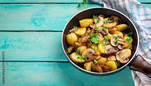 Fried potatoes with mushrooms, onions and parsley served in a frying pan with turquoise wooden background