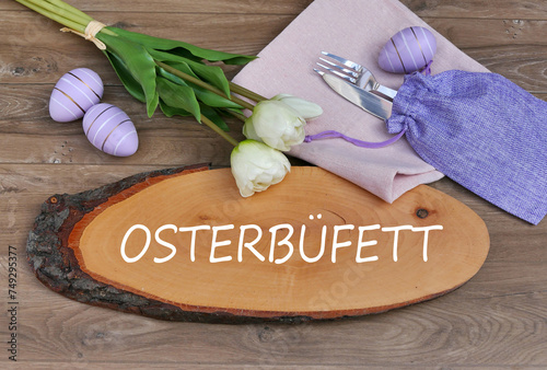 Der Text Oster-Buffet auf eine Baumscheibe geschrieben mit Besteck, Blumen und Ostereiern.	